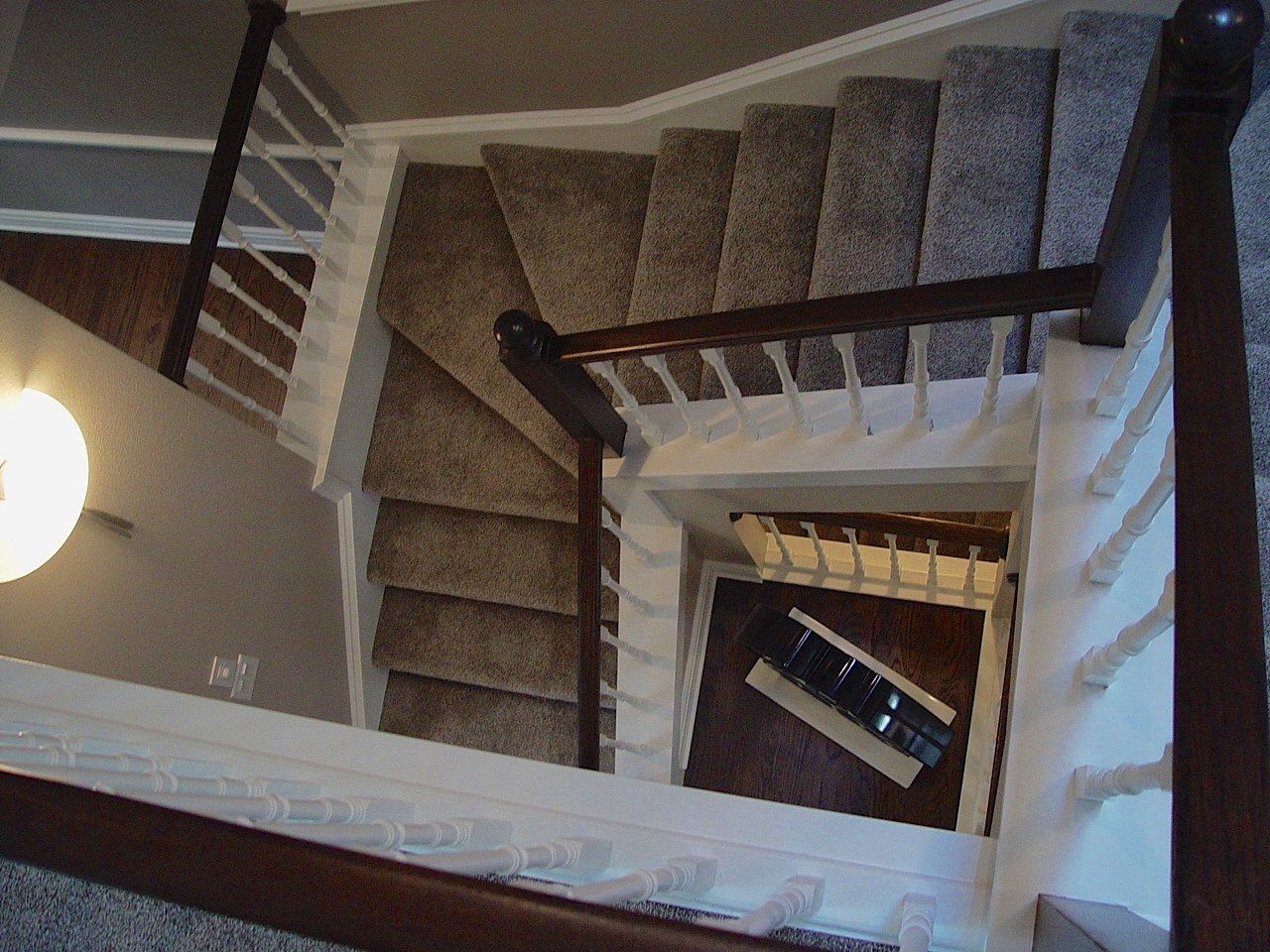 Staircase with carpeted steps, white railing, and wooden handrail, viewed from above.