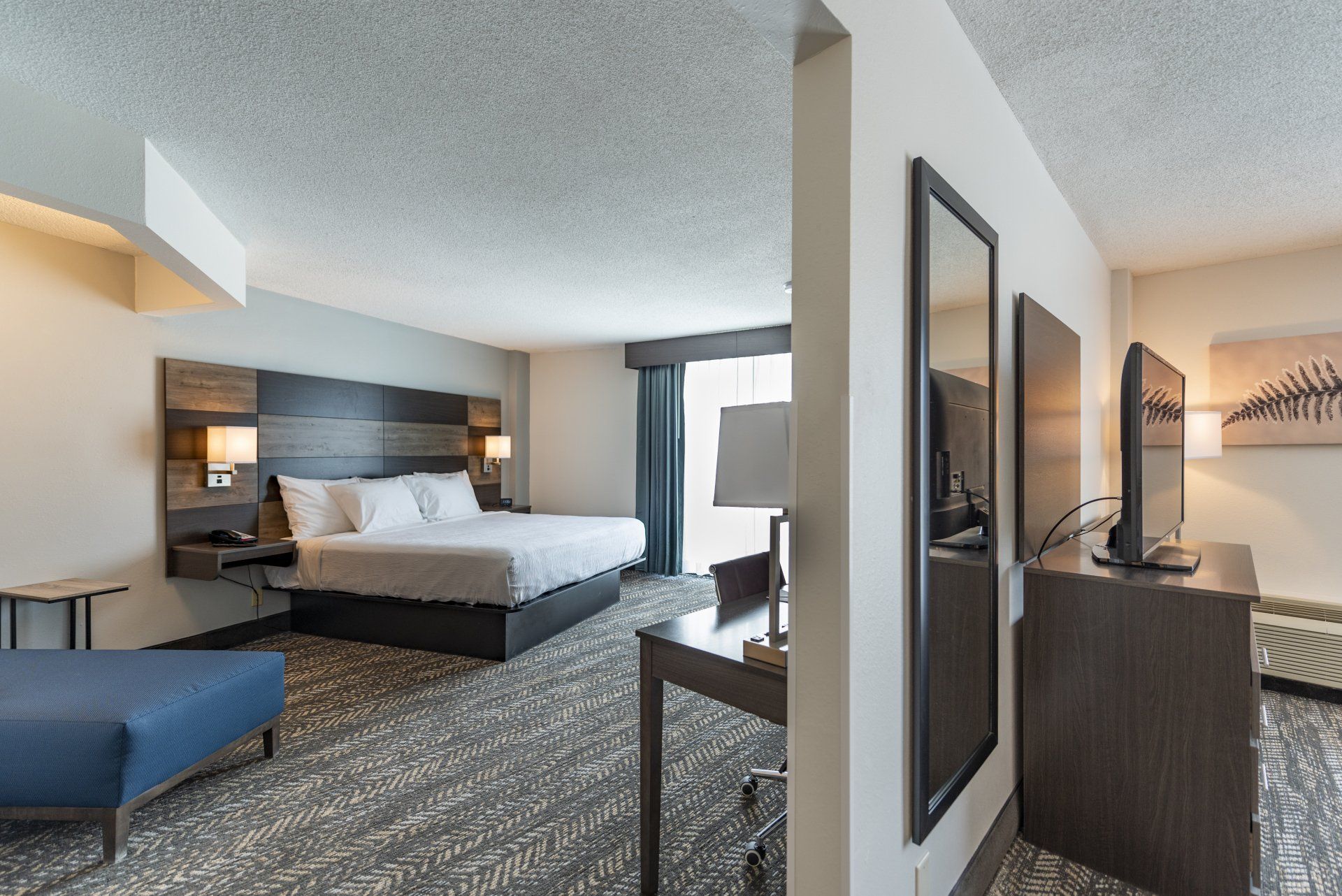Hotel room with a bed, desk, and TV; neutral colors, a modern design.
