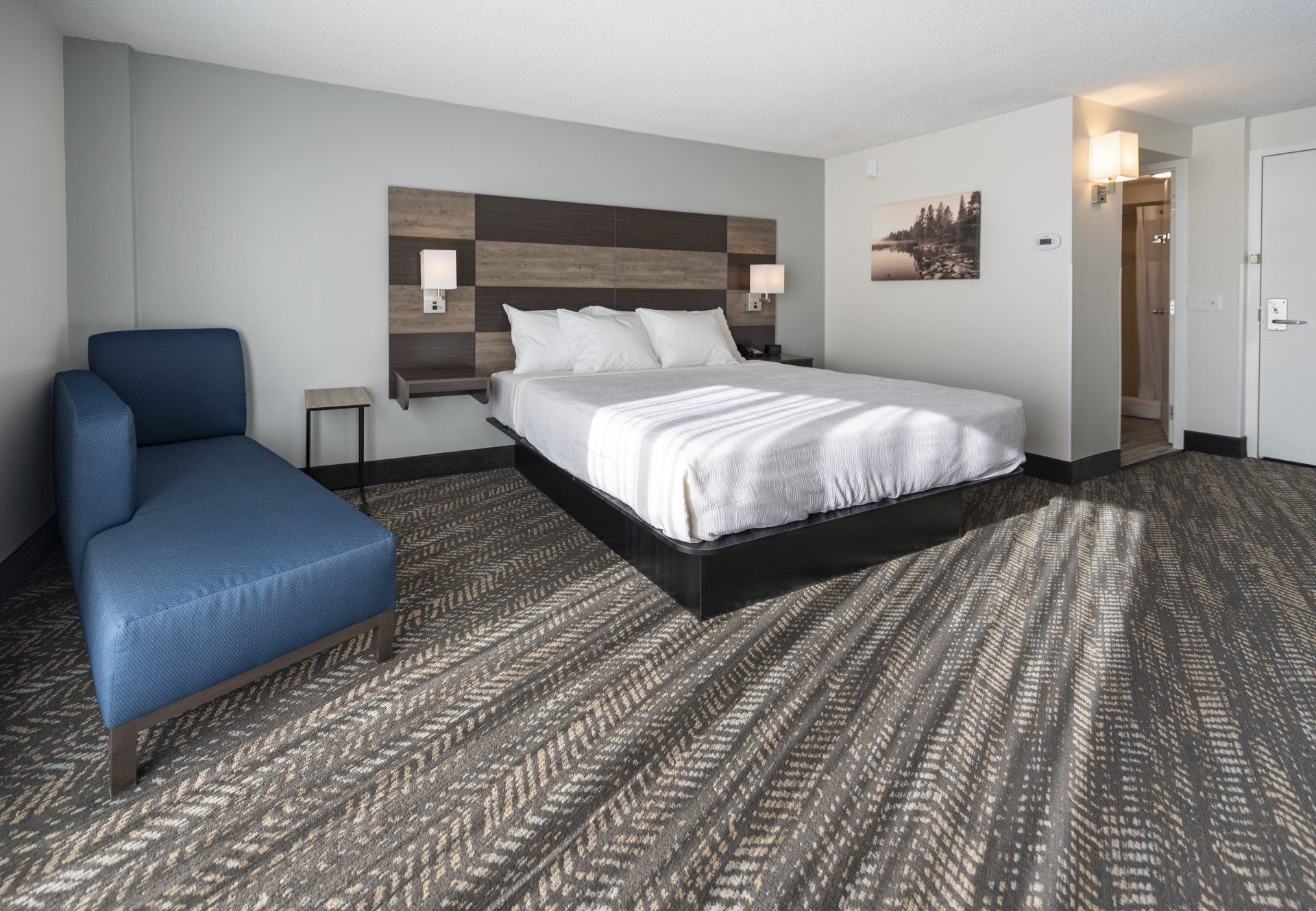 Hotel bedroom with a bed, blue chaise lounge, and carpet.
