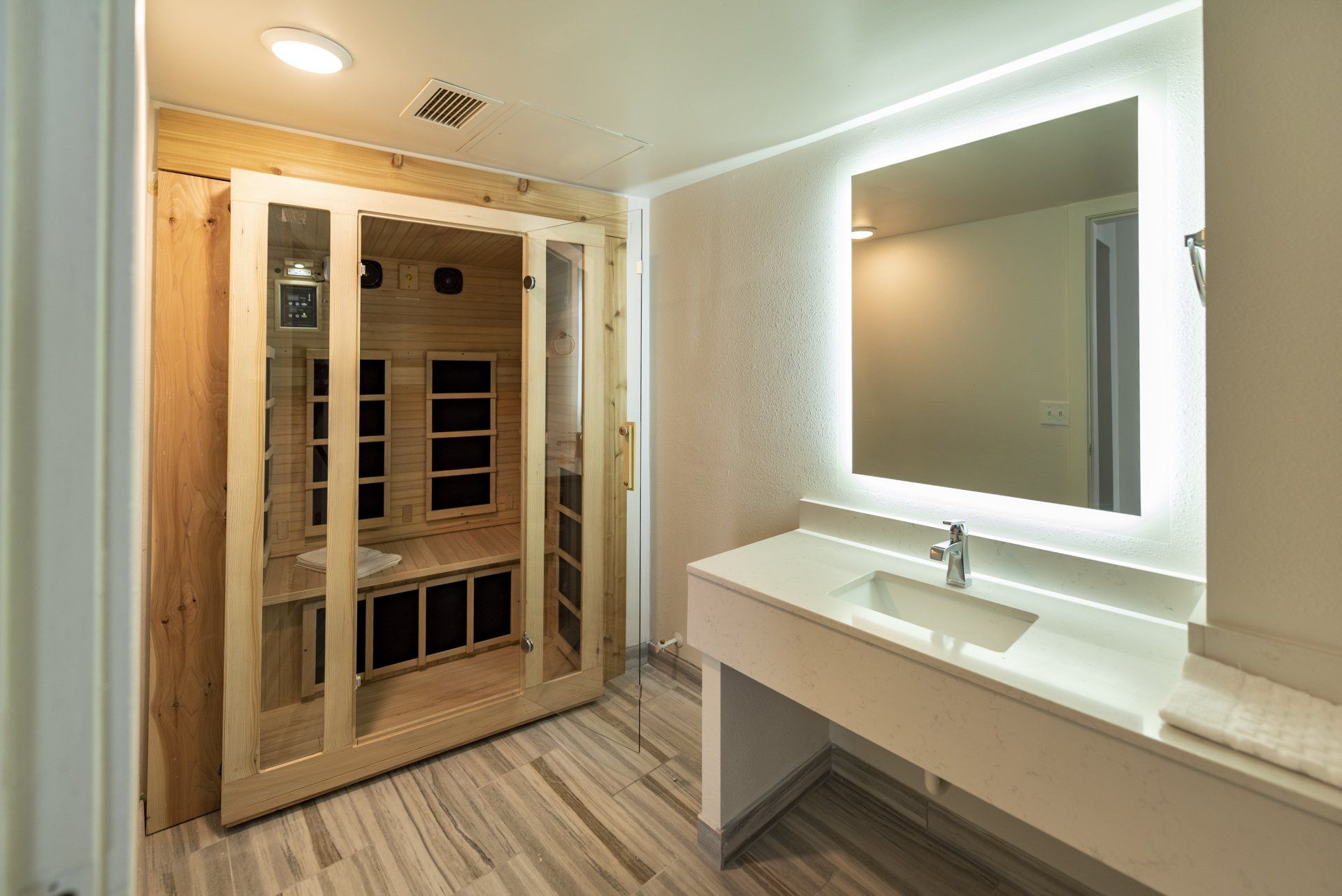 Bathroom with sauna. Light wood sauna next to white vanity with mirror. Light wood floor.