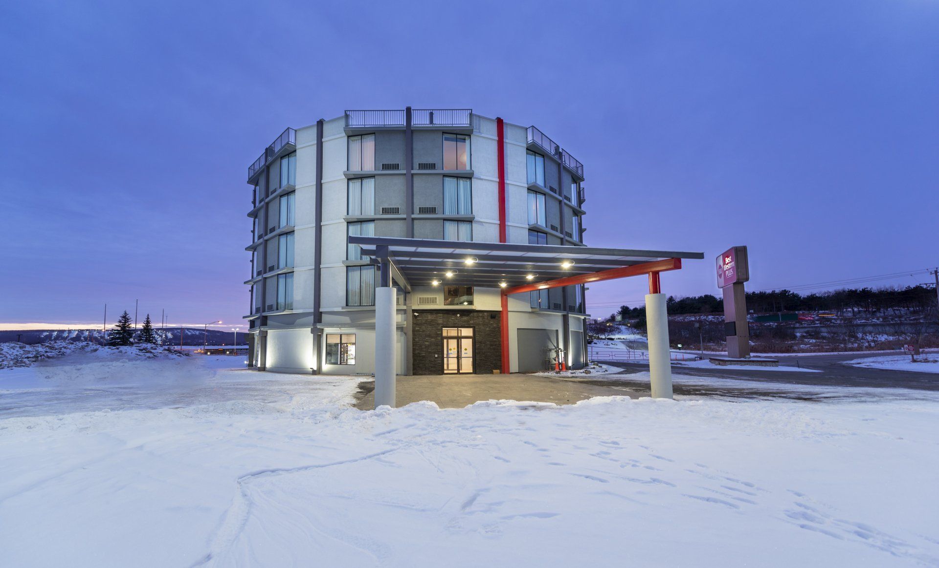 Round, multi-story building entrance with snow, dusk lighting.