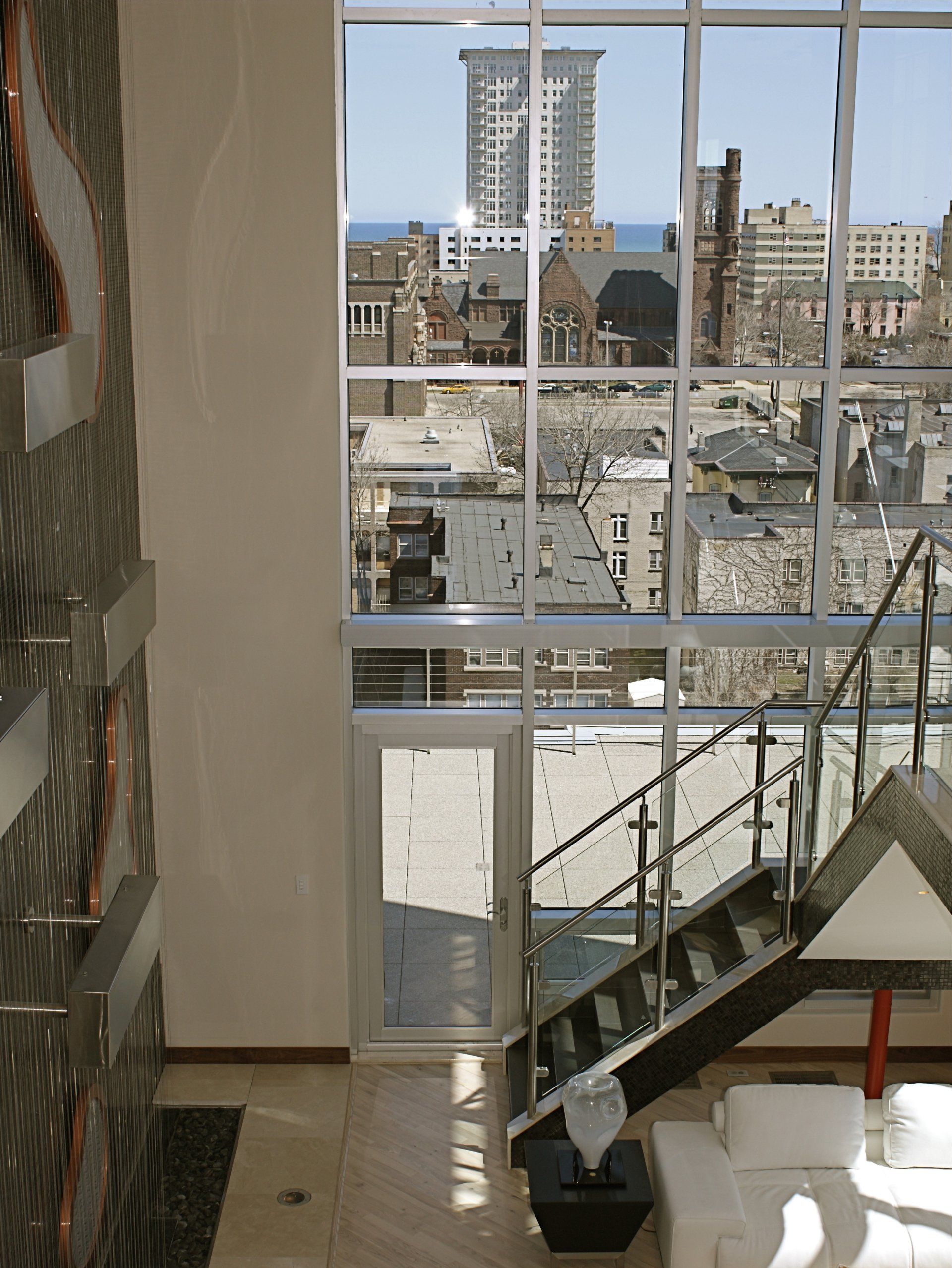 Interior view of modern loft with a cityscape through large windows and a staircase.