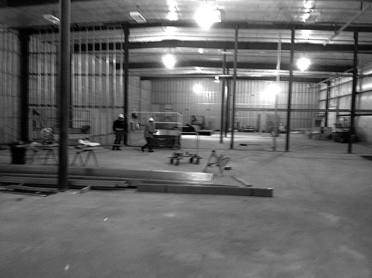 Interior of a building under construction, workers present, metal framing and concrete floor.