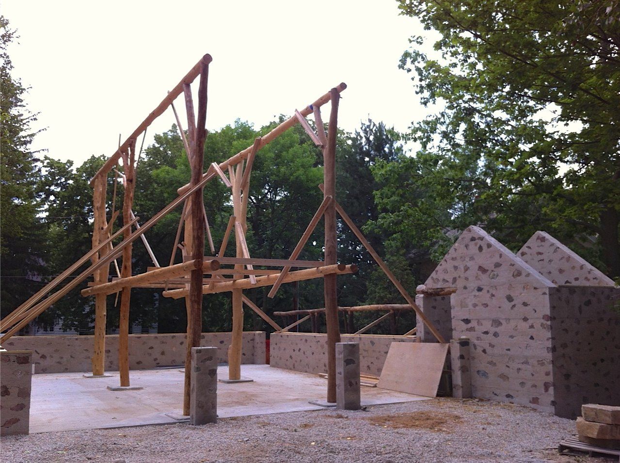 Construction site with wooden framework and stone walls in front of trees.