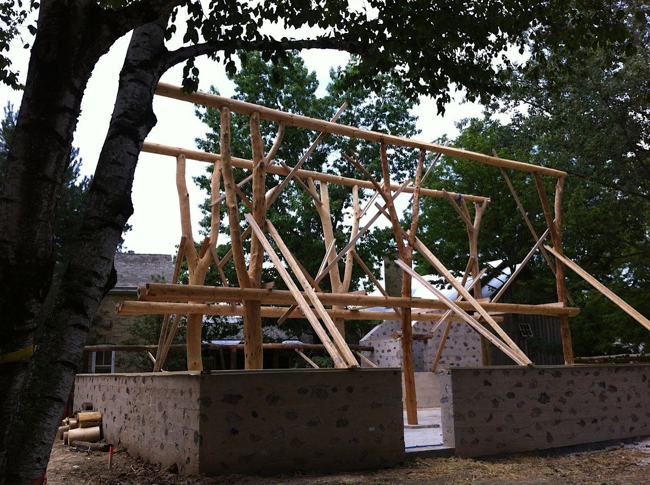 Wooden frame structure under construction on a concrete foundation, outdoors with trees.
