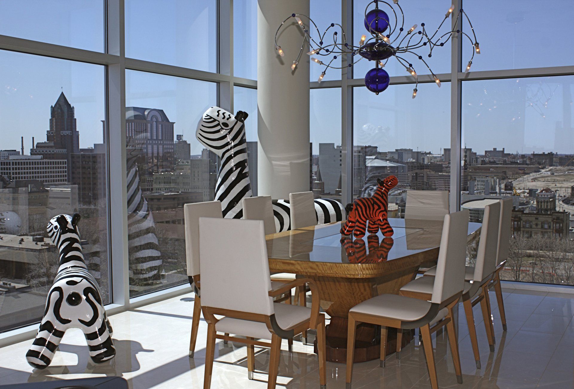 Dining room with zebra sculptures and a city view through large windows.