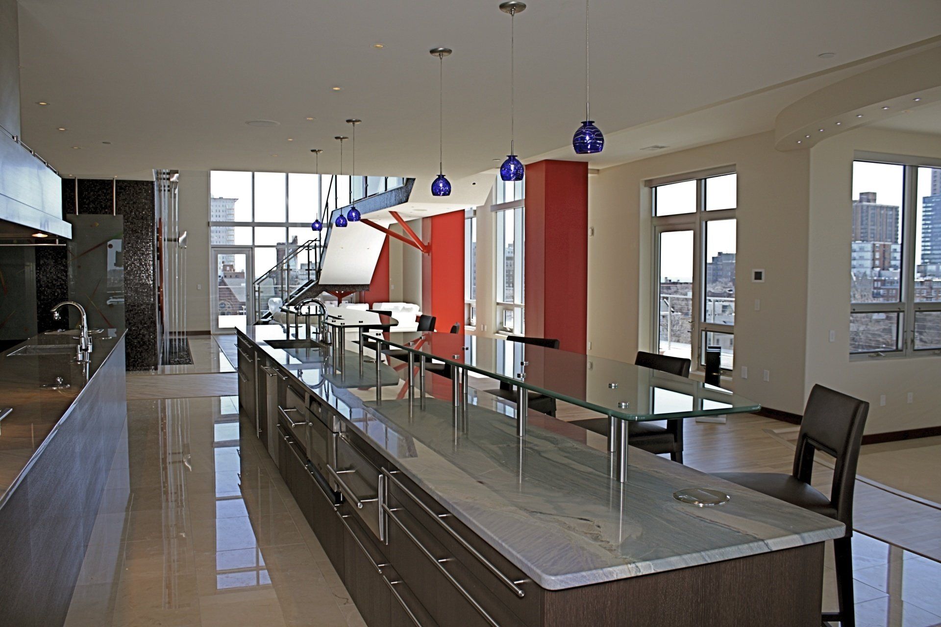 Modern kitchen with large island, stainless steel appliances, and city view through large windows.