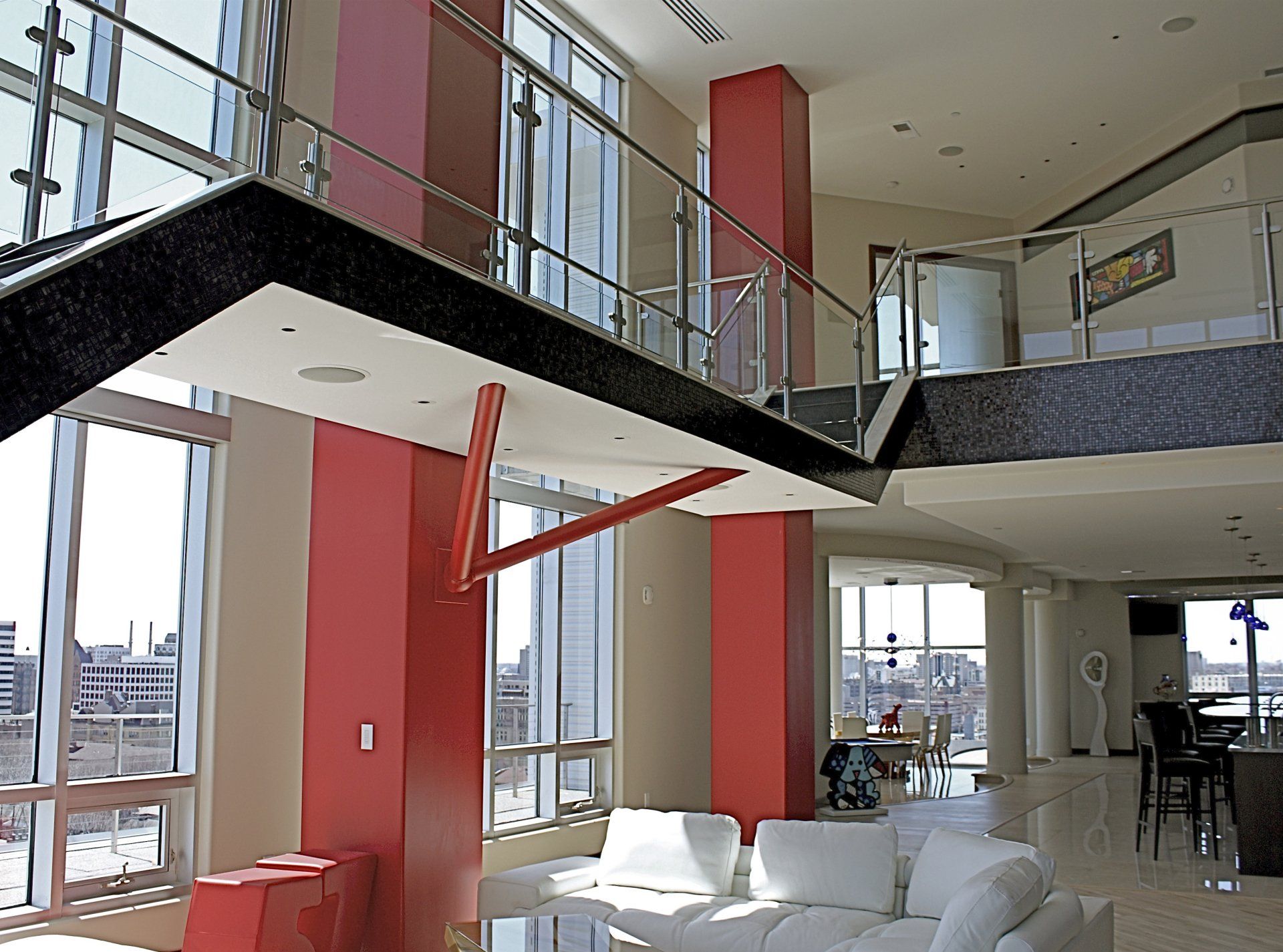 Modern interior with red pillars, large windows, a staircase, and a white sofa.