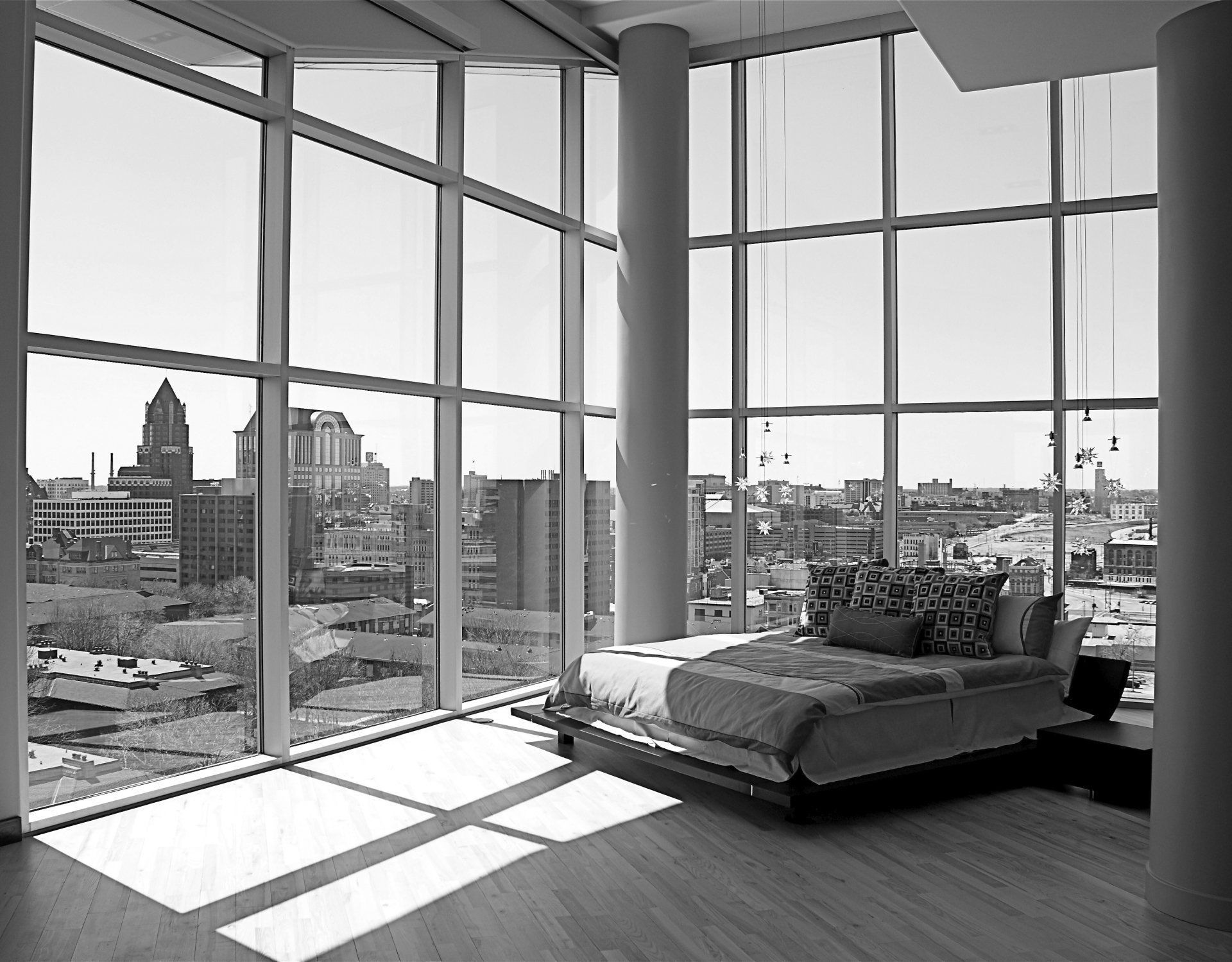 Bedroom with large windows, city view, bed, sunlight, and modern architecture.