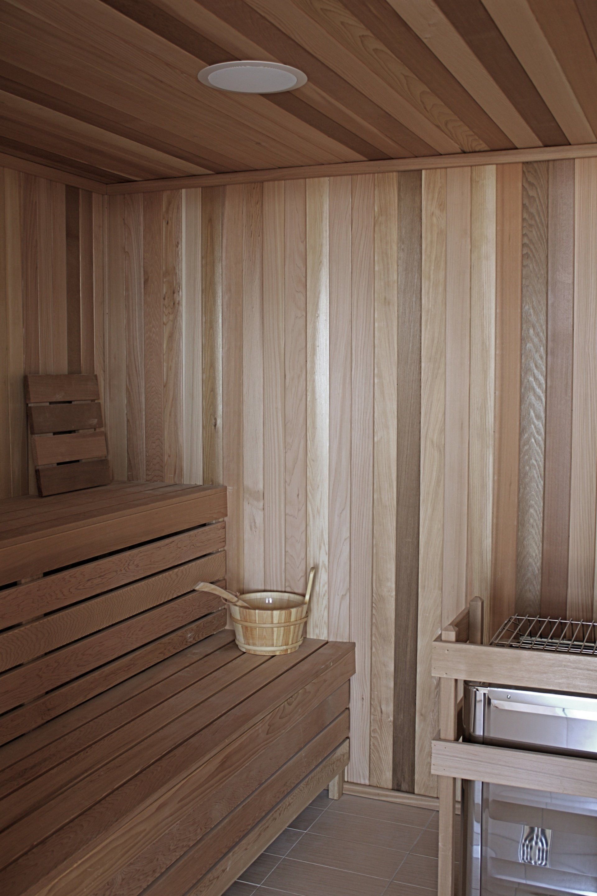 Interior view of a sauna with wooden benches, walls, and ceiling. A bucket and heater are visible.