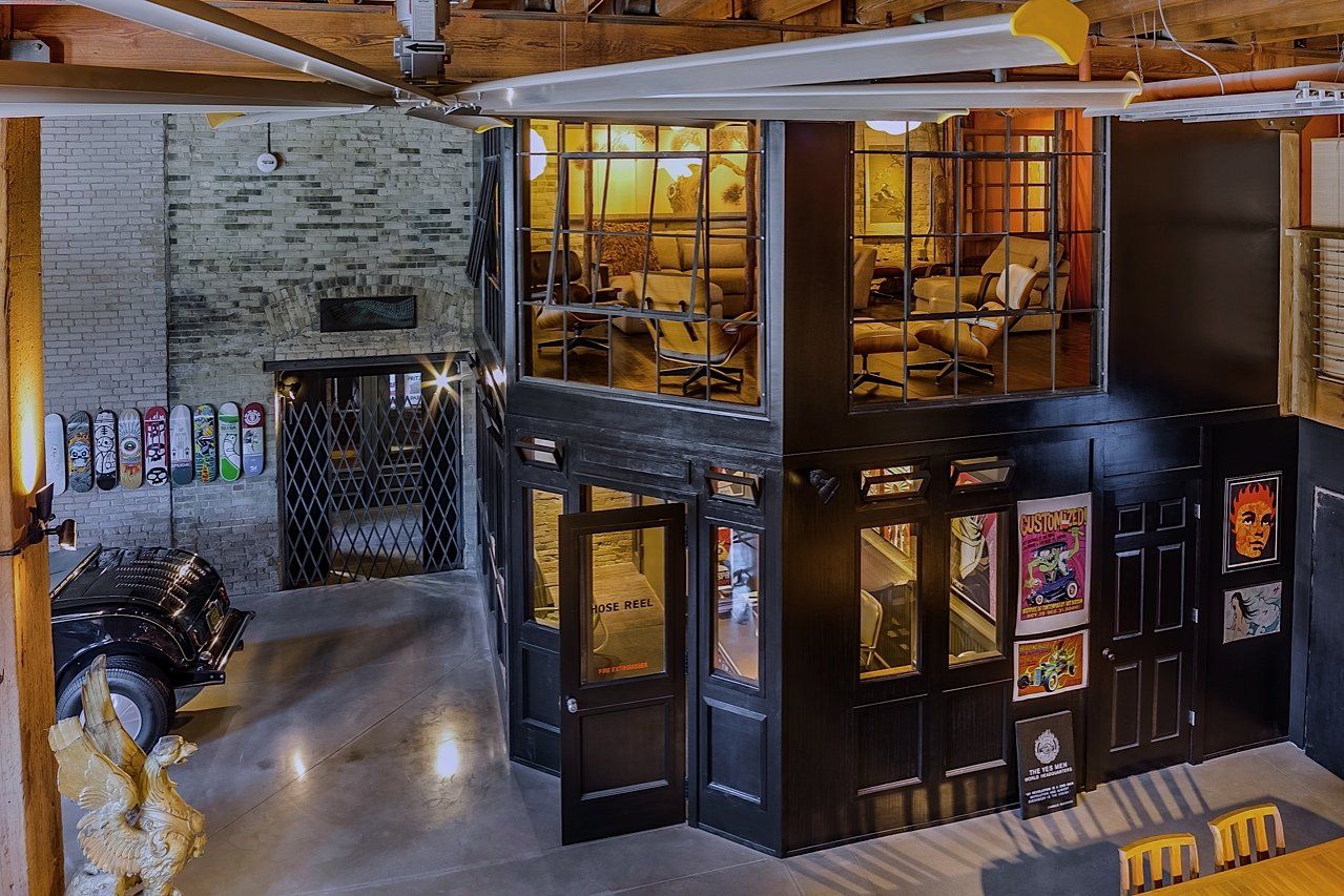 Interior with a two-story structure, black facade, glass windows, and posters. A light brick wall, skateboard deck display, and a ceiling fan are also visible.