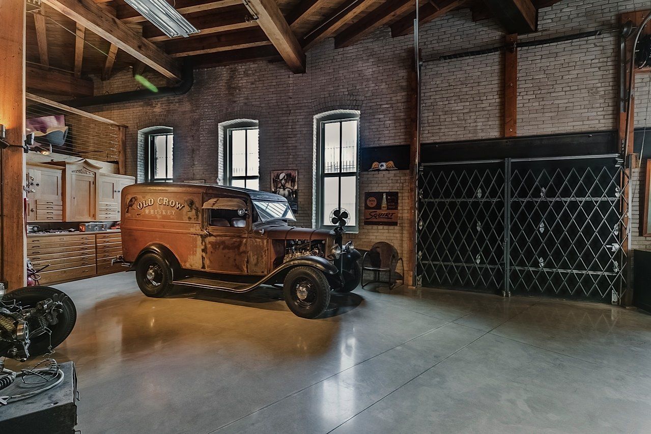 Vintage, rusty car in a brick-walled warehouse with high ceilings, arched beams, and large windows.