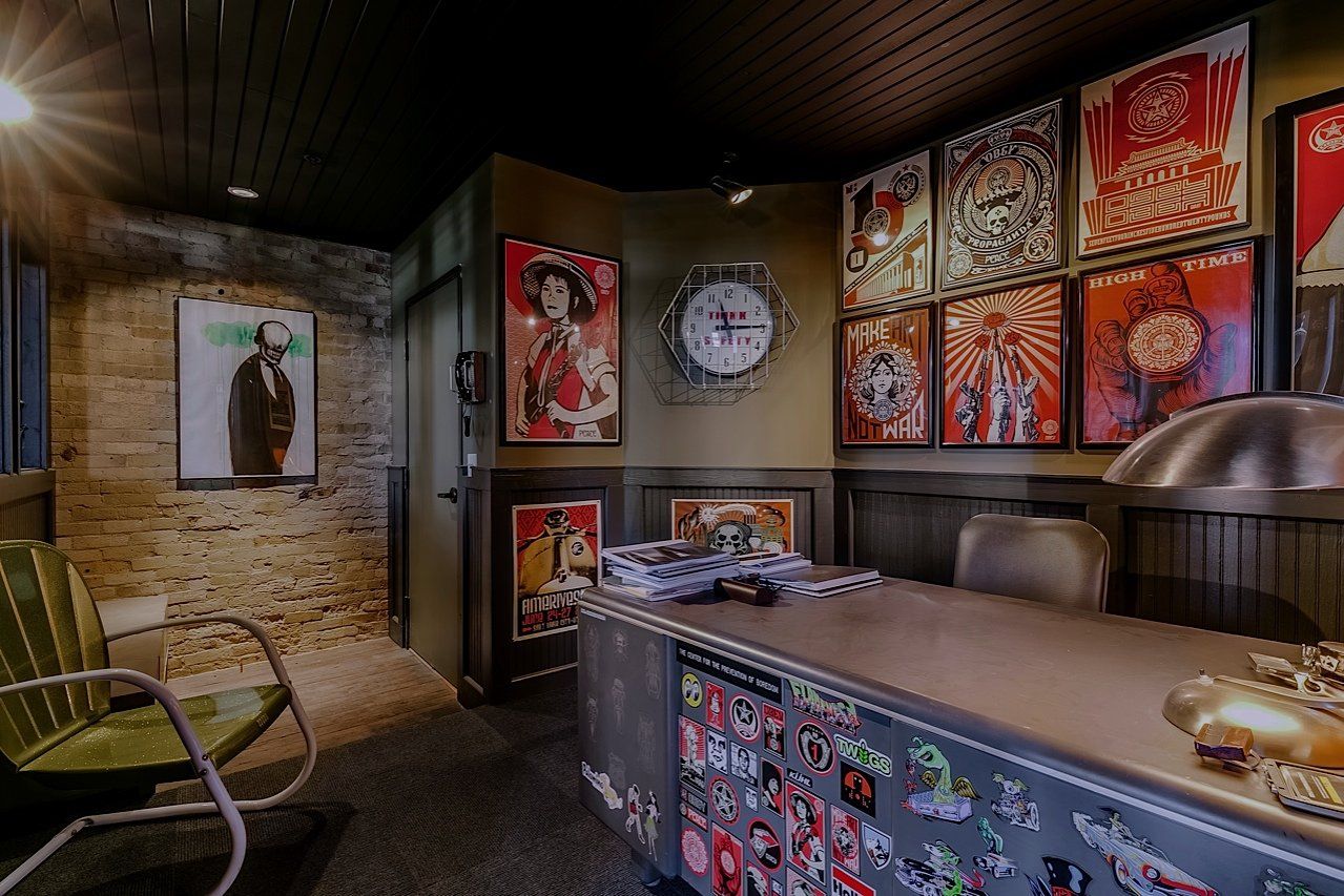Office with desk, posters, brick wall, green chair, clock, and dim lighting.