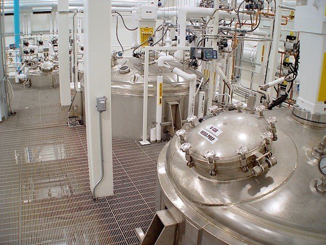Industrial plant interior with large stainless steel tanks, pipes, and walkways.