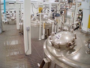 Industrial facility interior with metal tanks, pipes, and grated flooring.
