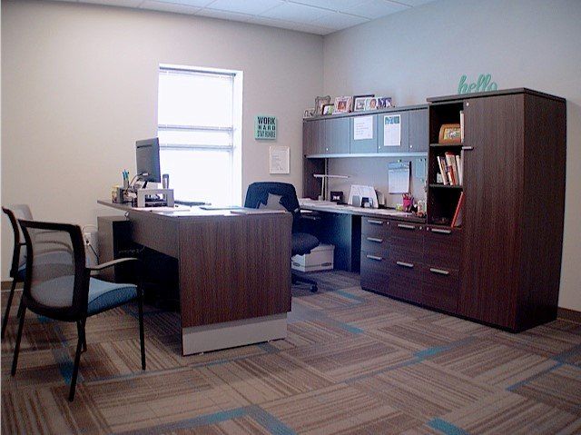 Office with desk, cabinets, chair, and window. Brown desk, blue chair, neutral walls.