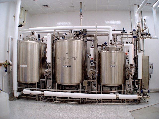 Stainless steel tanks and piping in a sterile room, likely for processing liquids.