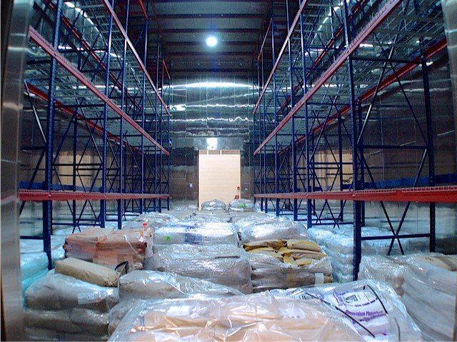 Empty warehouse interior with metal shelving and wrapped pallets of goods.