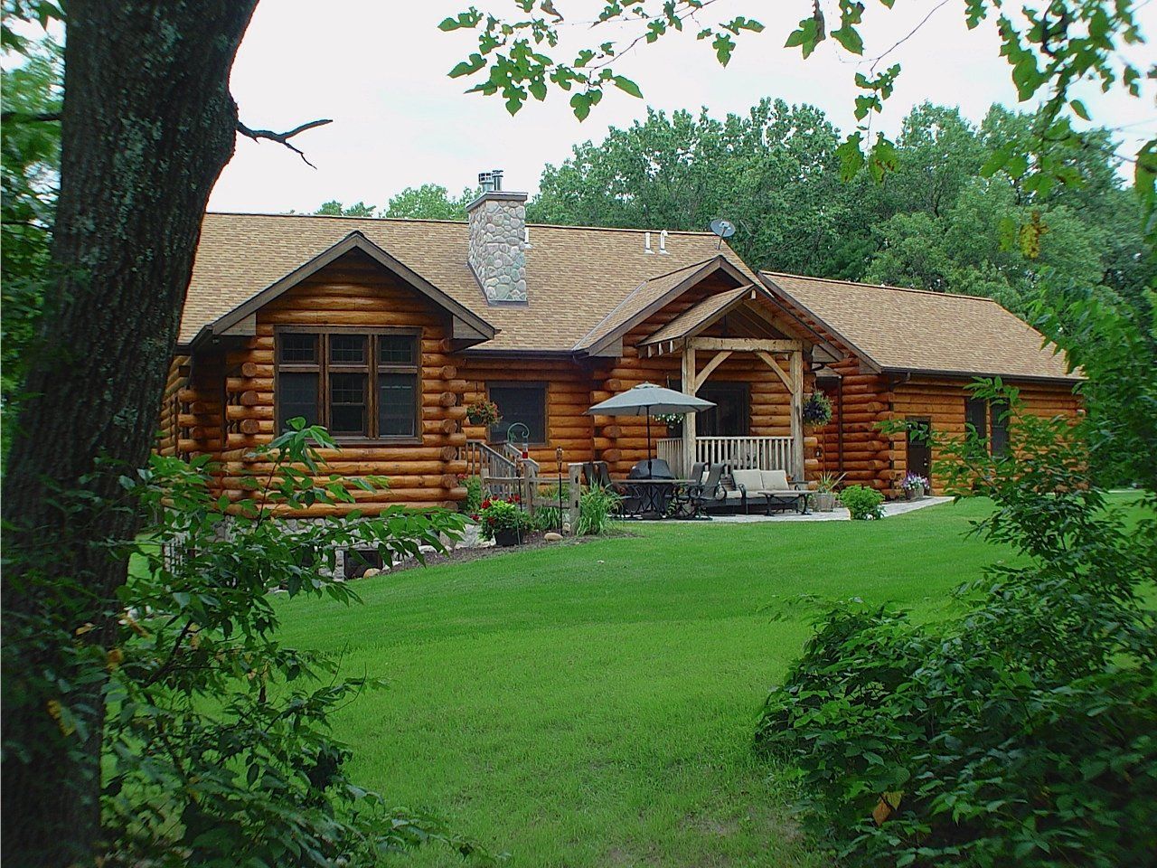 Log cabin with a covered porch, surrounded by green grass and trees.