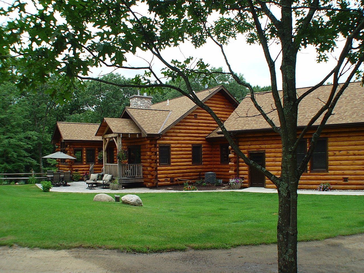 Log cabin with wood roof, green lawn, trees, and outdoor seating.