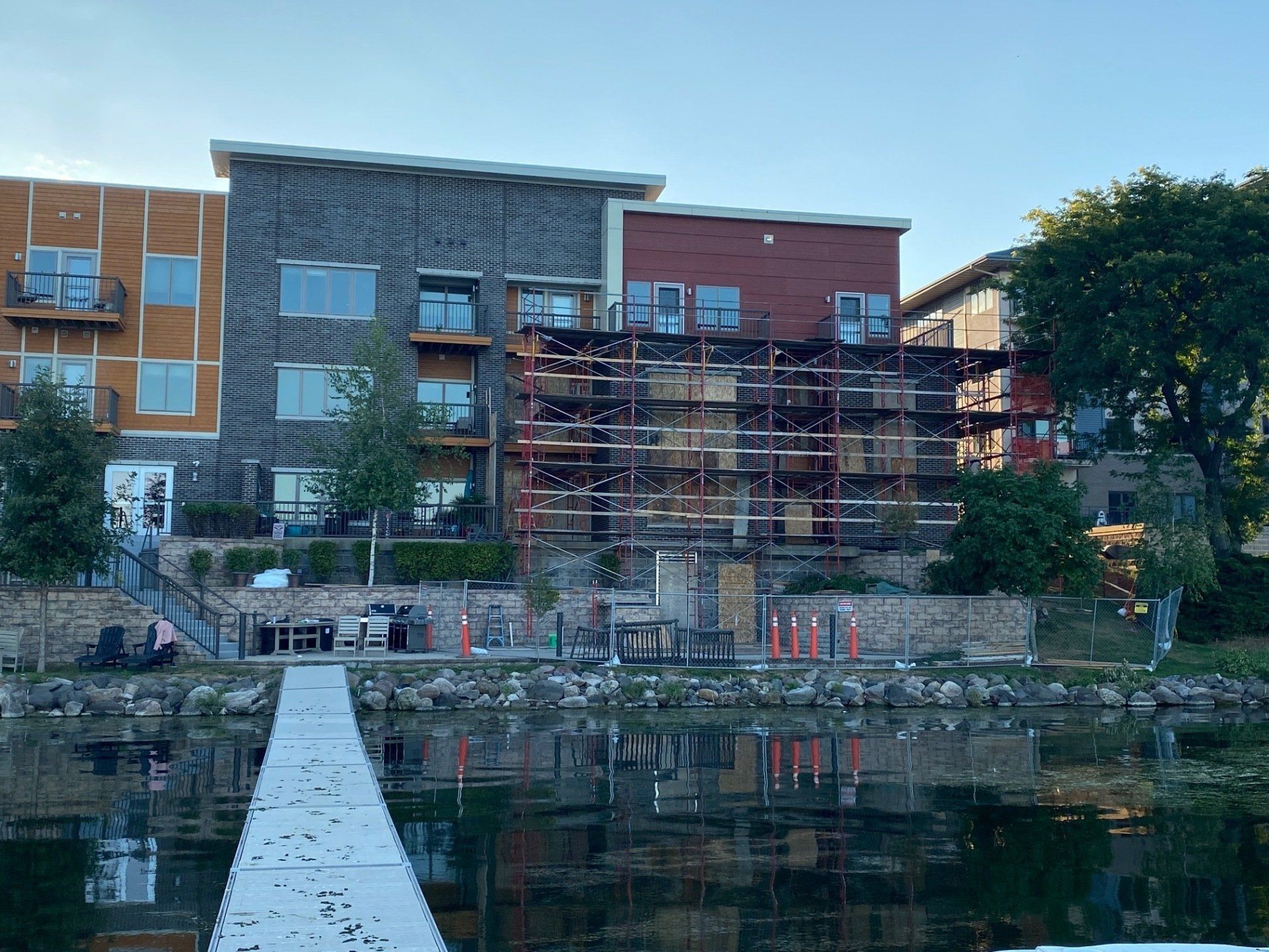 Buildings with a pier over water; scaffolding on the middle building, orange traffic cones on the water's edge.