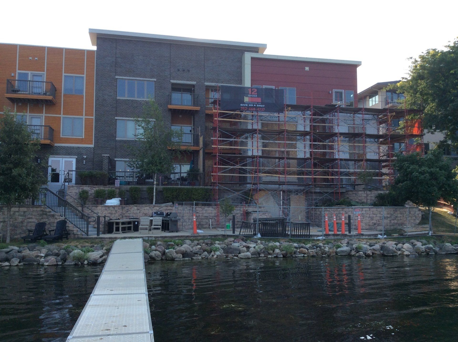 Multi-story building with scaffolding, dock on water. Construction zone near waterfront.