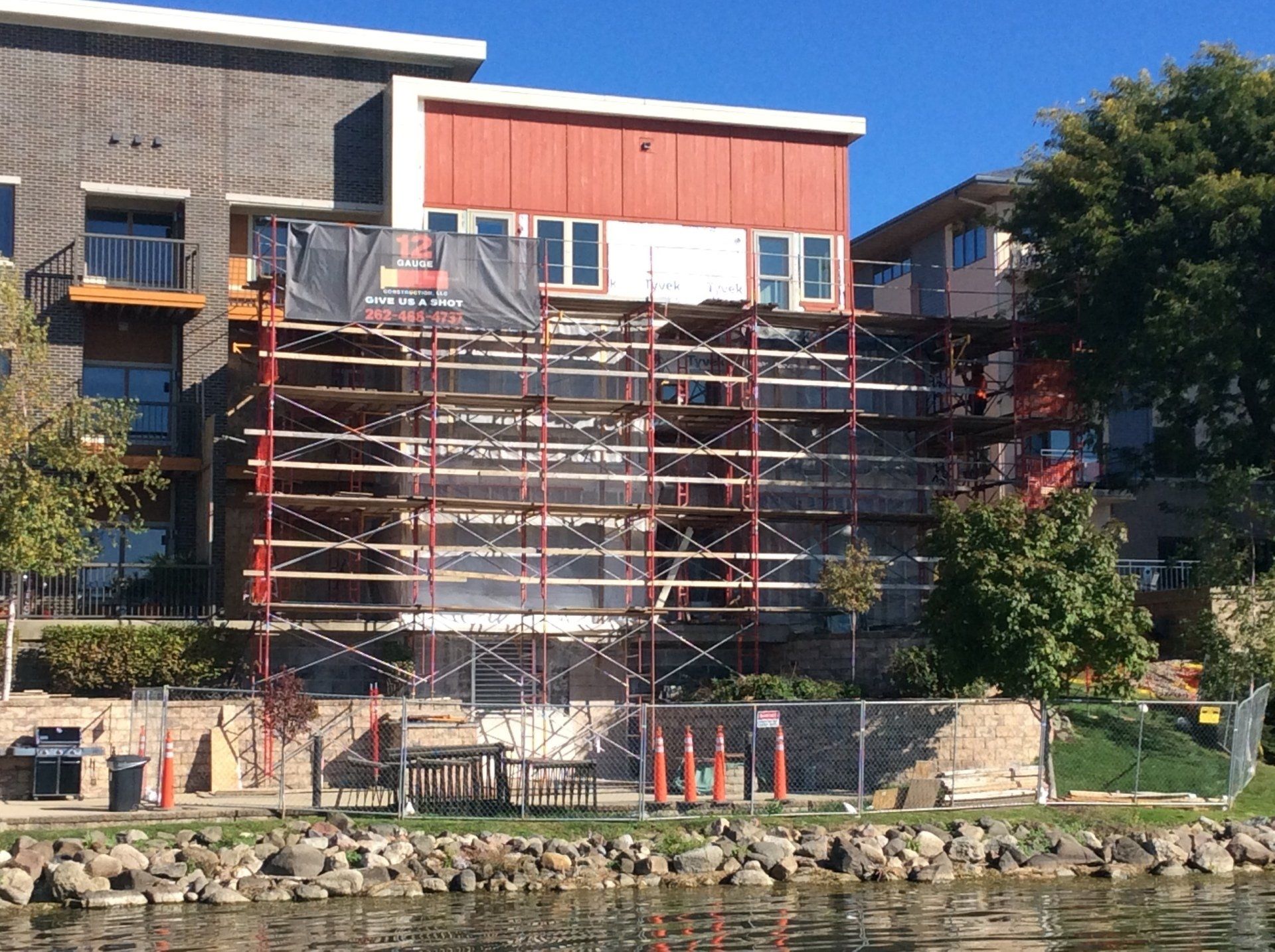 Building under renovation with scaffolding on the exterior. Red and gray siding. Fenced waterfront.