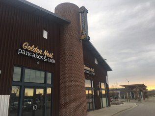 Golden Nest Pancakes & Cafe restaurant exterior. Brown building with sign and brick pillar against a cloudy sky.