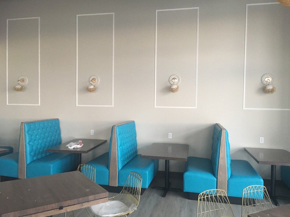 A restaurant with teal booths, small tables, gold chairs, and wall decorations.