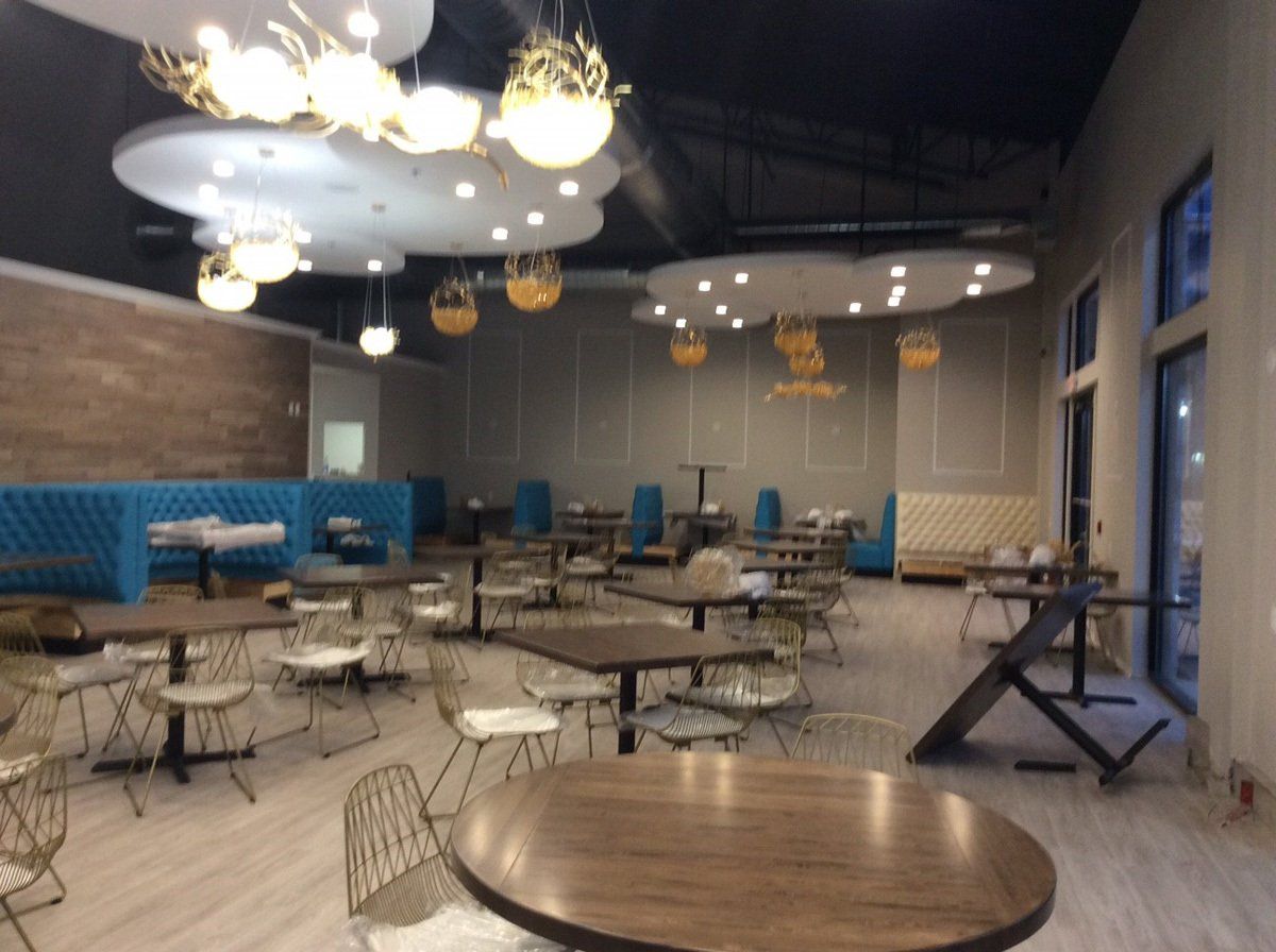 Restaurant interior with tables, chairs, booths, and decorative cloud-shaped ceiling lights. Blue and tan color scheme.