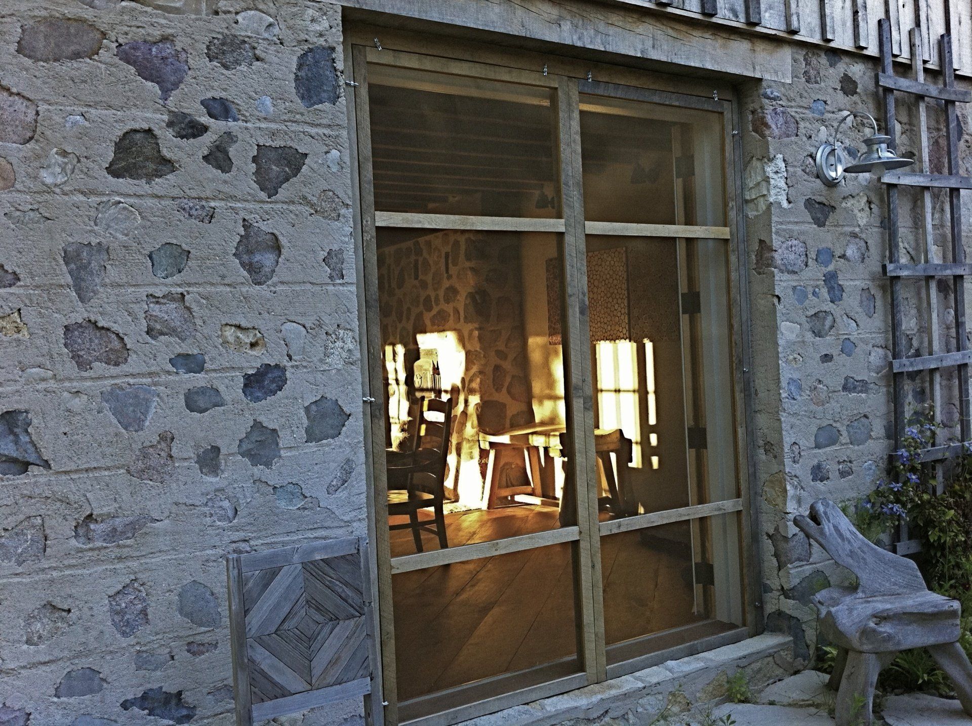Stone building with a wooden screen door. Sunlight reflects off interior furniture.