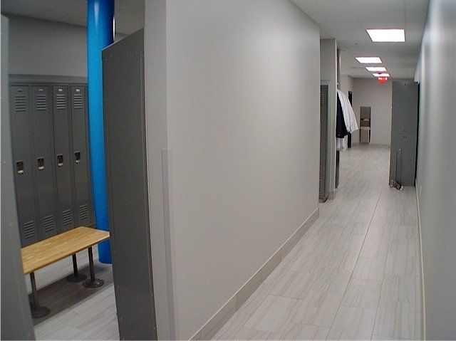 A hallway in a locker room with lockers, benches, and a light blue support beam.