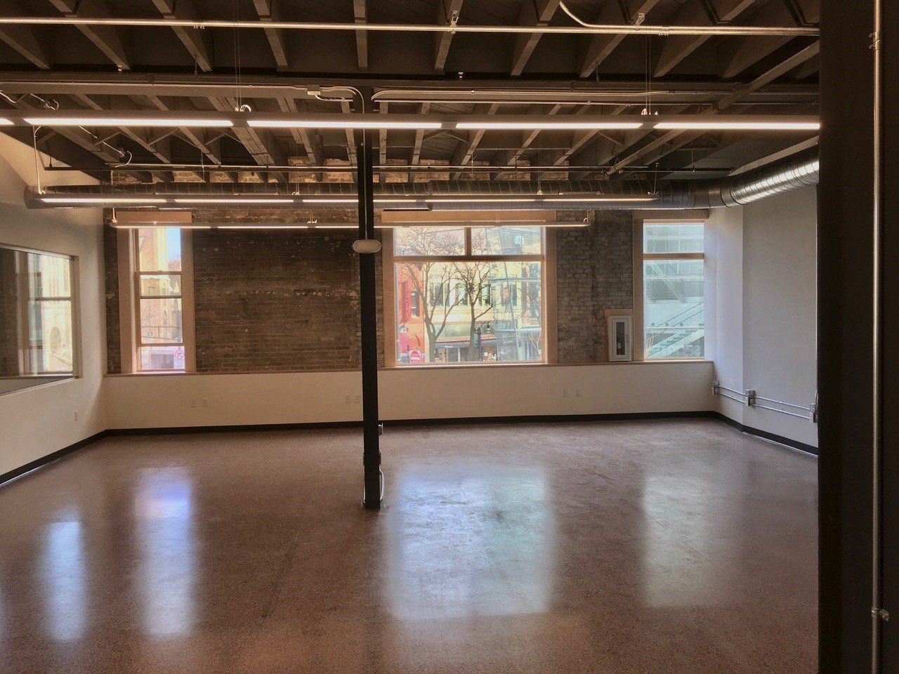 Empty room with windows, exposed brick, and a shiny floor.