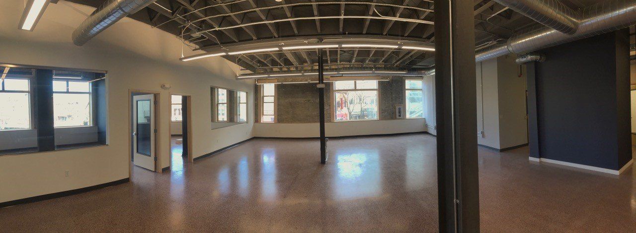 Interior view of a large, empty room with high ceilings, exposed beams, and multiple windows.