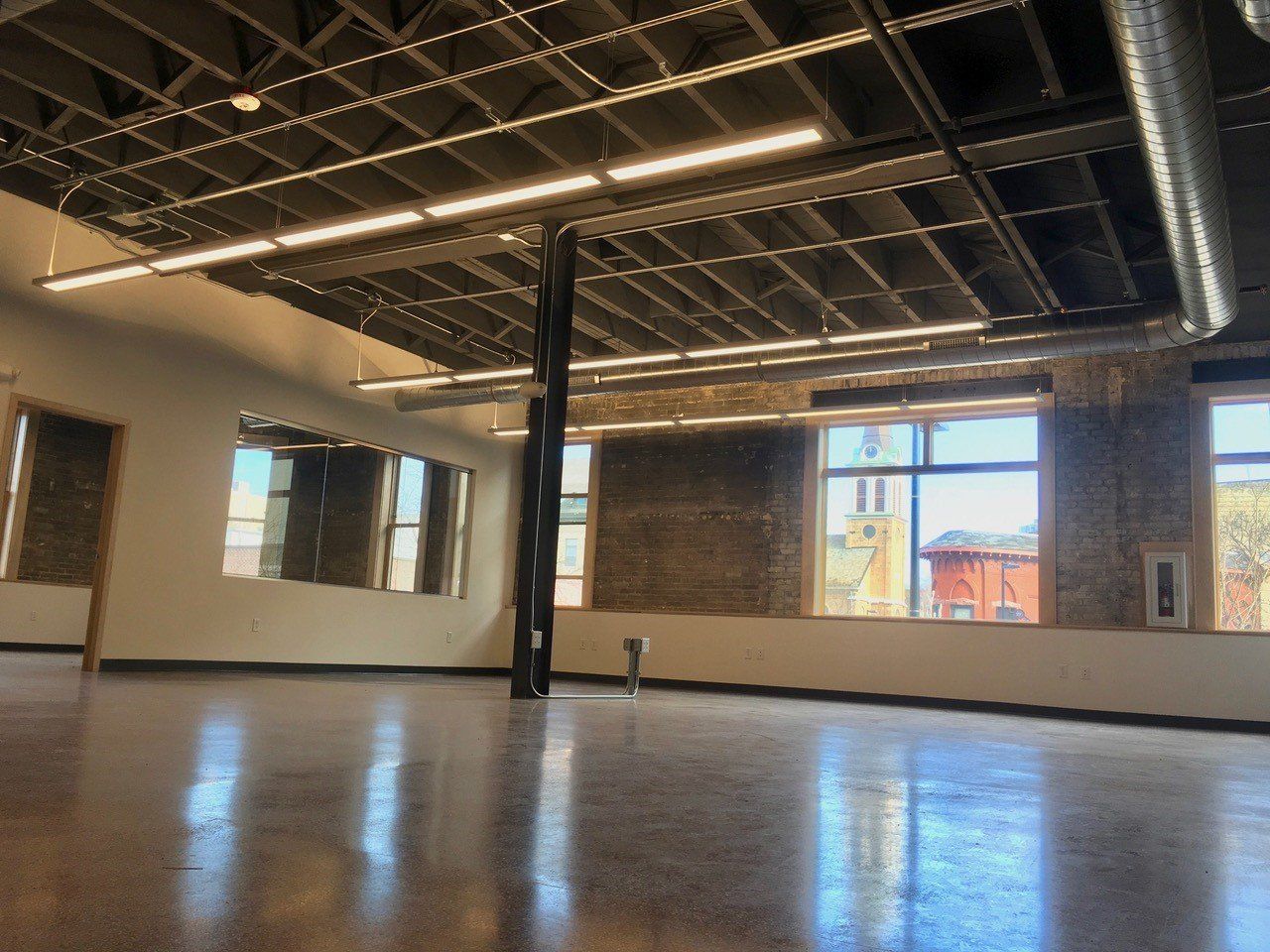 Empty dance studio with polished concrete floor, exposed brick, and large windows.