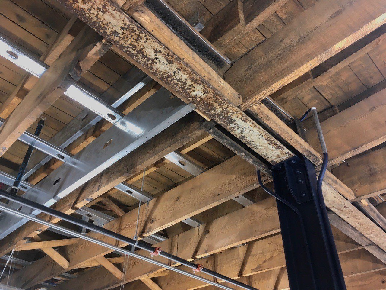 Rusty metal beam supports a wooden ceiling in an industrial setting.