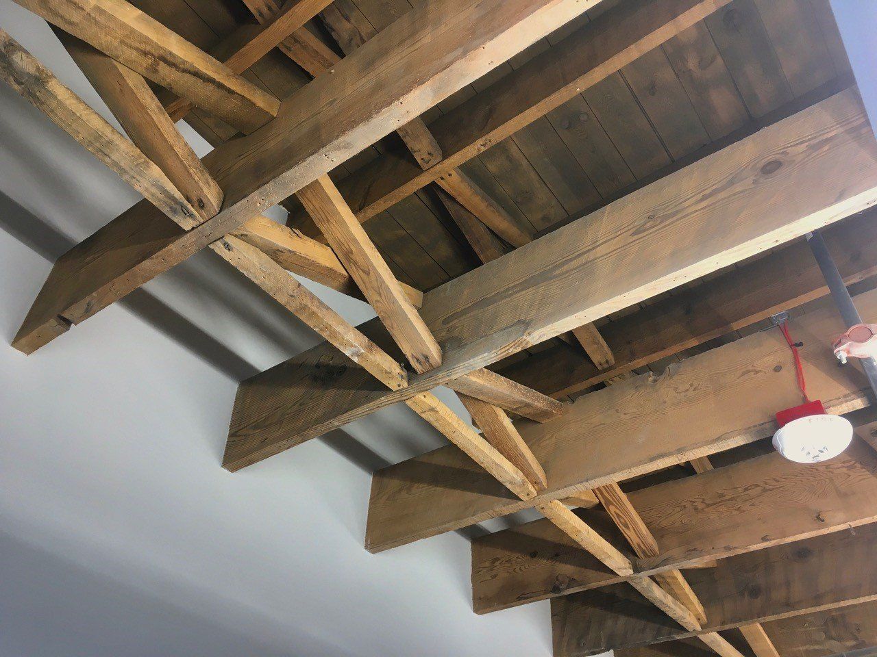 Wooden rafters and support beams on a ceiling; gray walls.