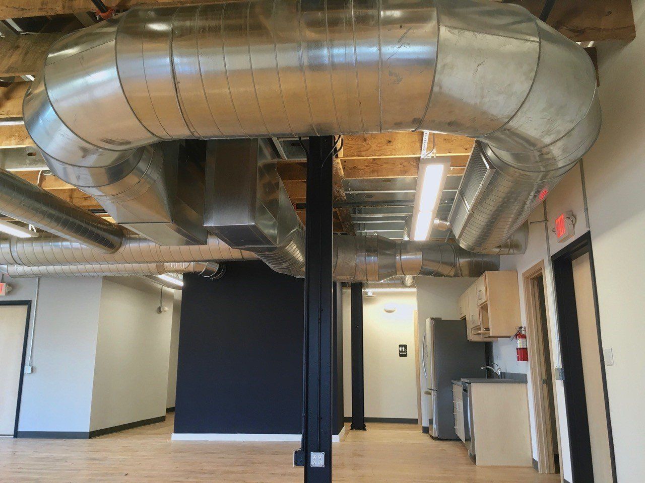 Interior view of a modern office space, featuring exposed ductwork, support beams, and a kitchenette.