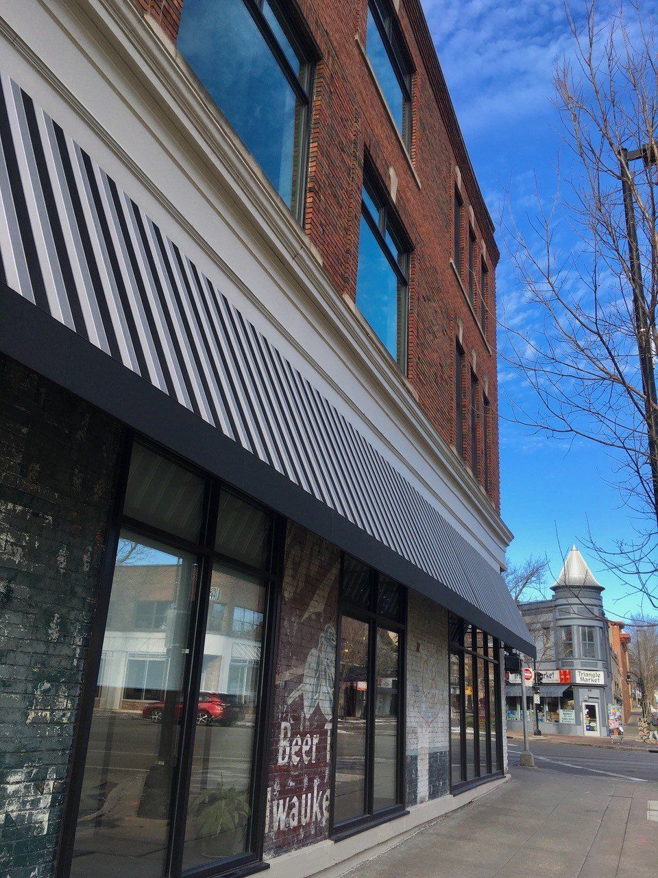 Brick building with large windows and a striped awning on a sunny day.