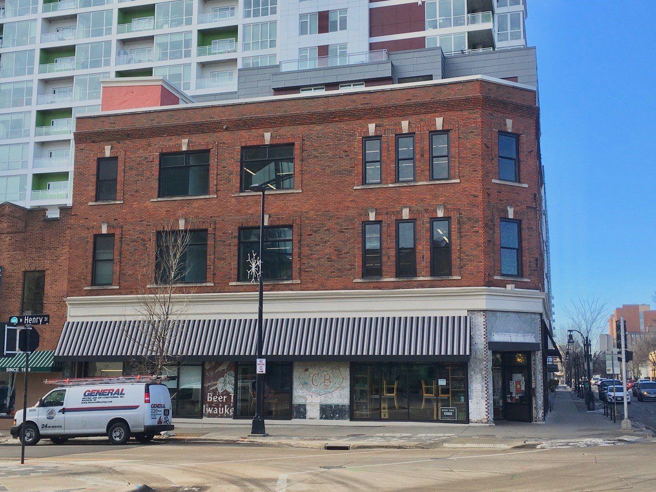 Brick building with black and white striped awning; white van parked in front.