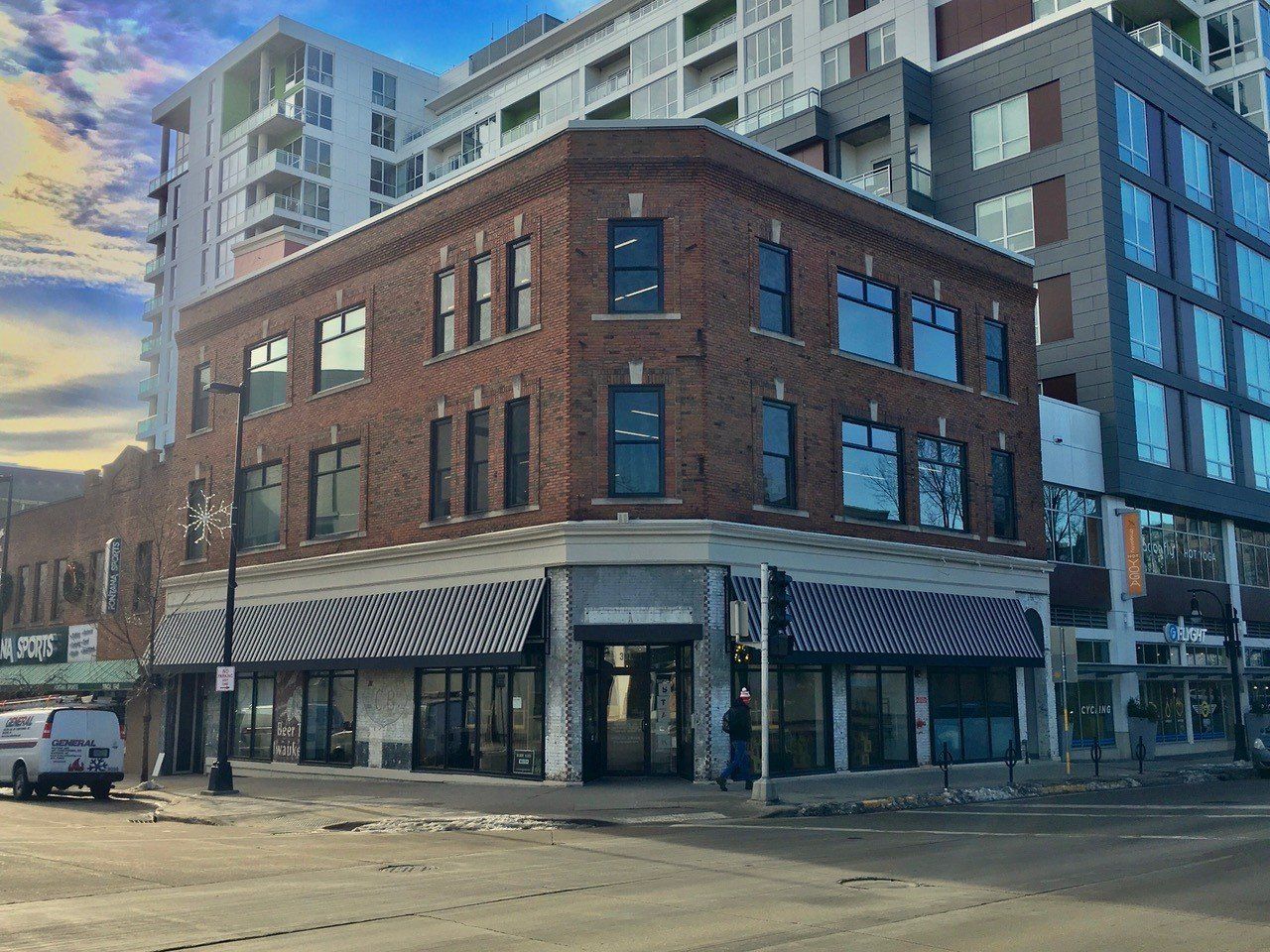 Brick building on a corner with awnings. Modern buildings in the background, street in the foreground.