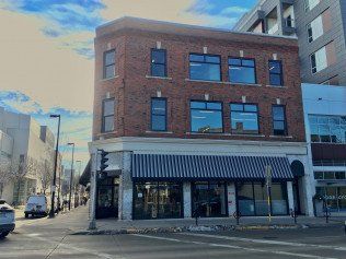 Three-story brick building on a street corner, with striped awning over ground-floor windows.
