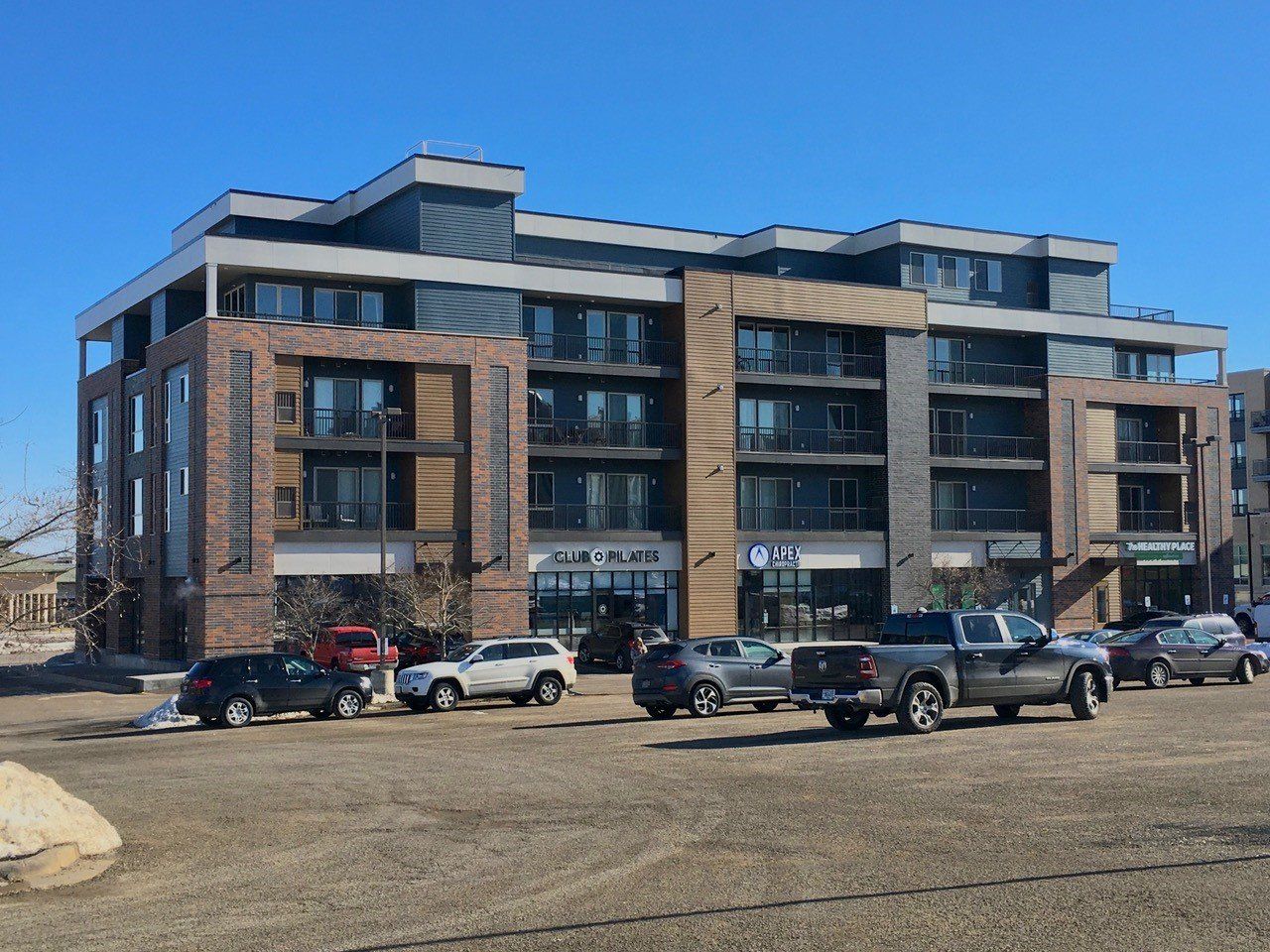 Modern multi-story building with shops and parked cars on a sunny day.