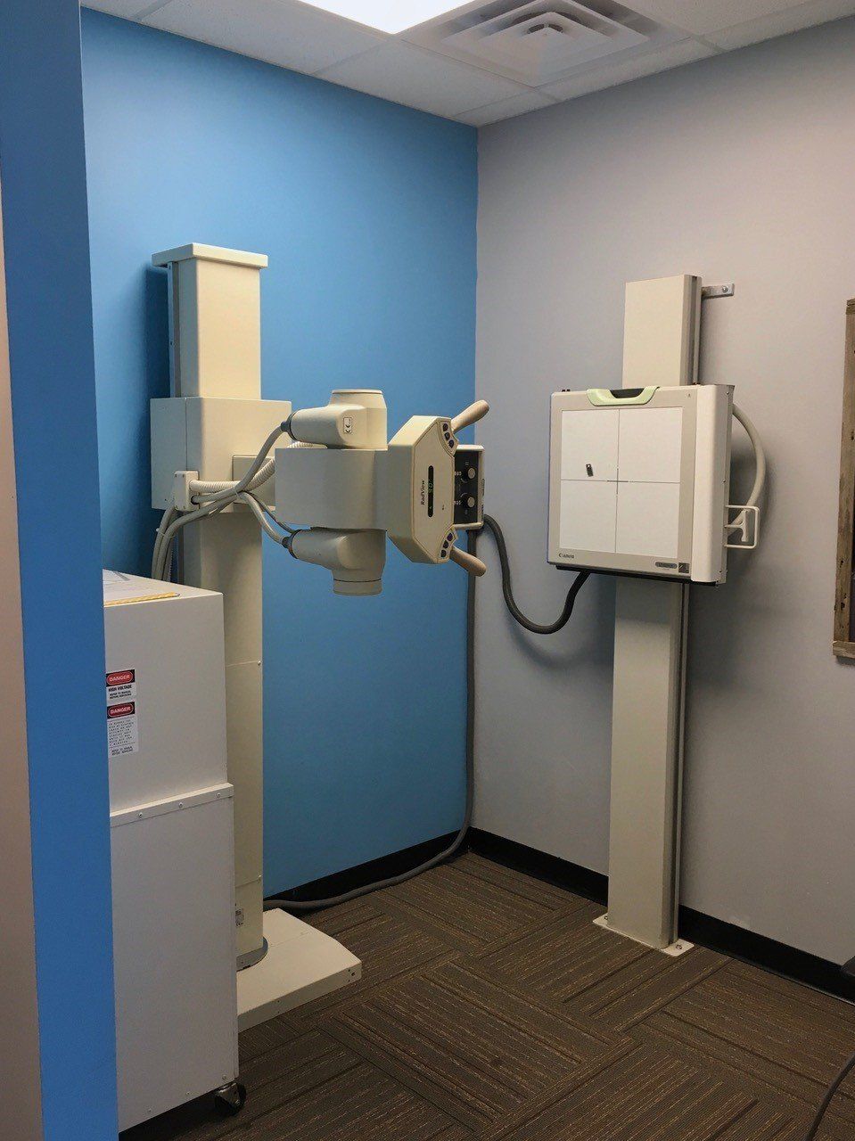 X-ray machine in a medical examination room, featuring a white machine against blue and gray walls.