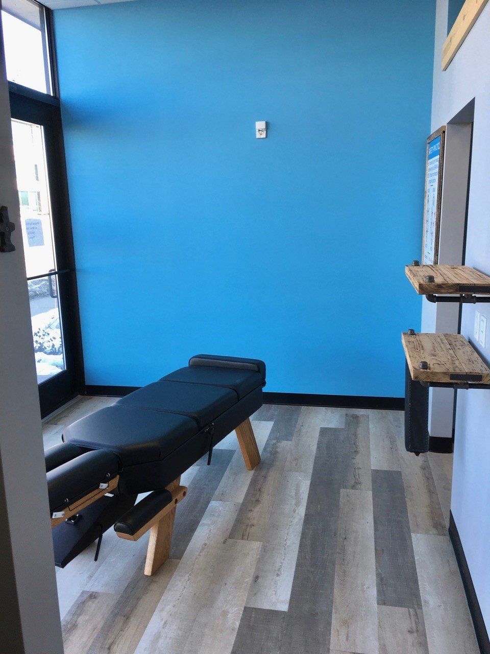 Chiropractic room with blue wall, treatment table, and wood shelves.