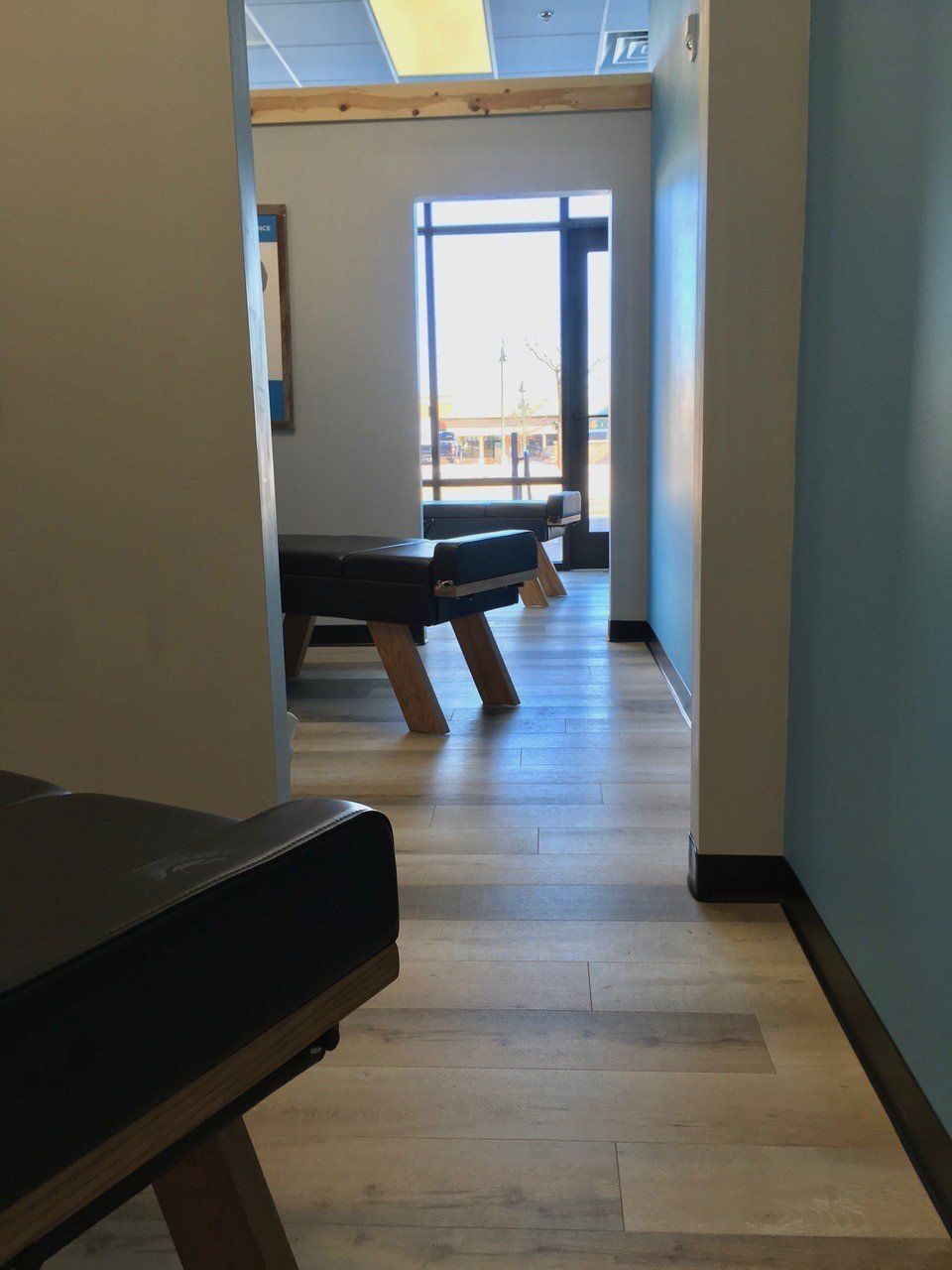 Hallway with exam tables, leading to a window. Light-colored wood floor, blue and white walls.