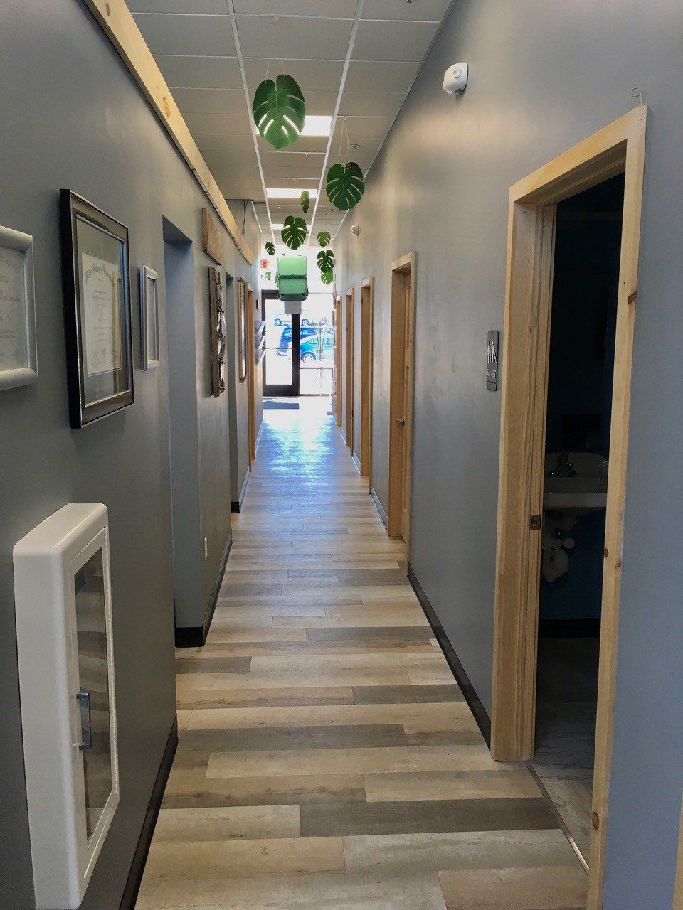 Long hallway with wooden doors, grey walls, and hanging green leaf decorations.