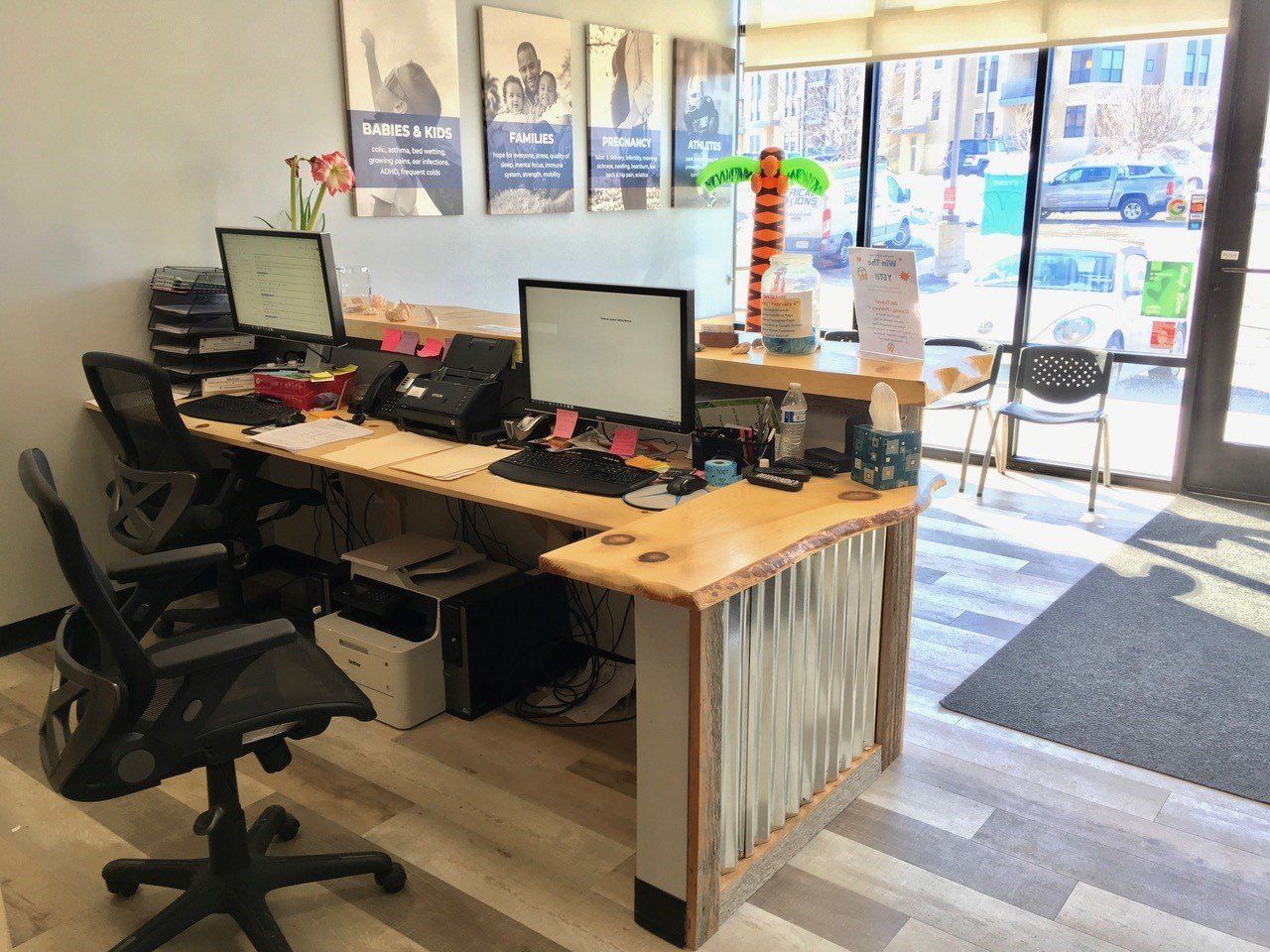 Office reception desk with computers, chairs, and a palm tree decoration.