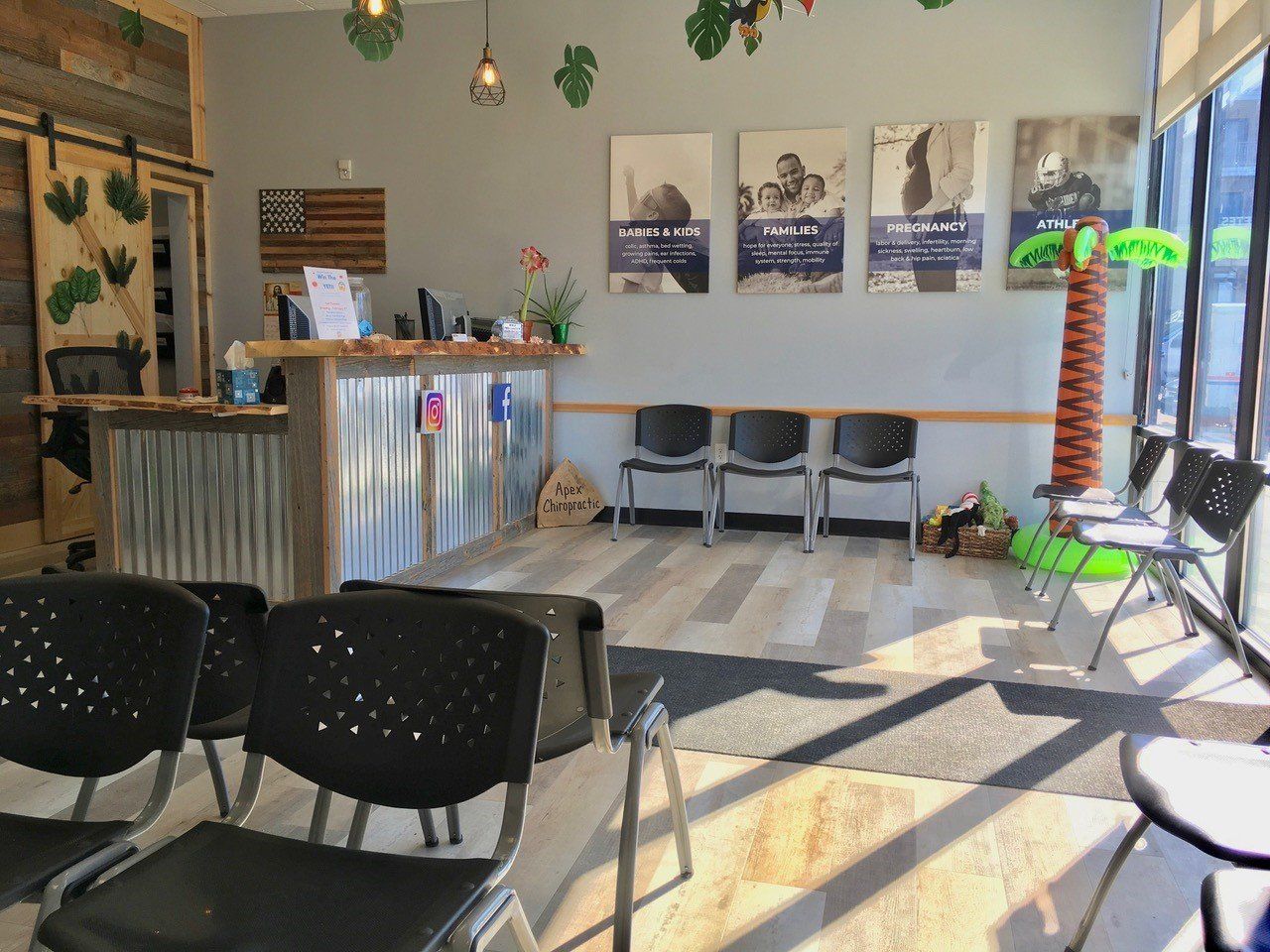 Reception area: desk, chairs, posters, wood and corrugated metal accents, palm tree decoration, and American flag.