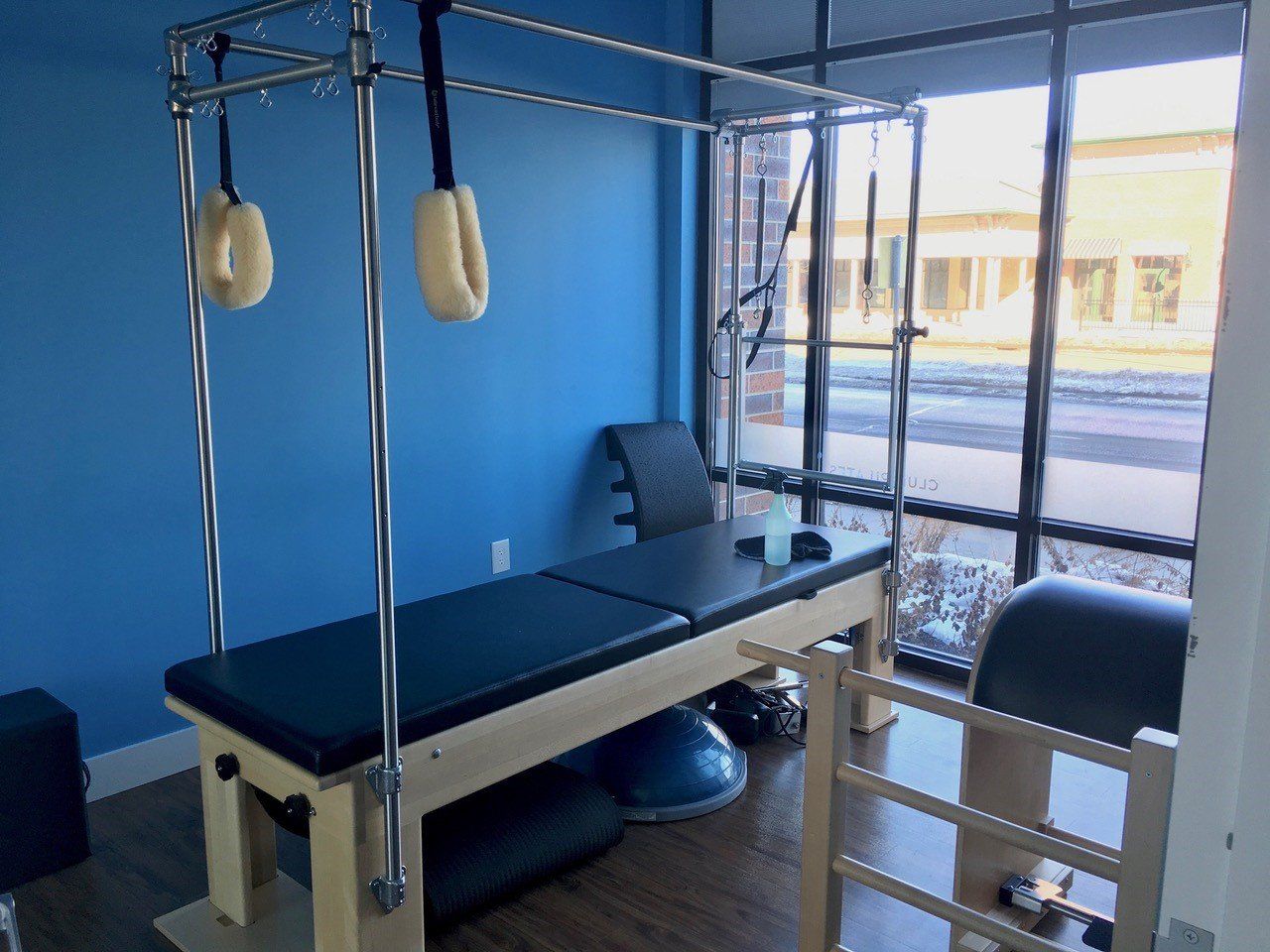 Pilates reformer in a bright blue room with a large window overlooking a street.